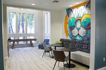 A room with a table and chairs and a mural of a cat wearing glasses.